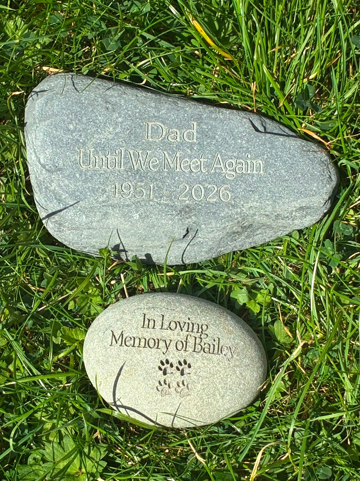 Two personalised natural memorial stones for a loved one and a pet, engraved and displayed together on grass