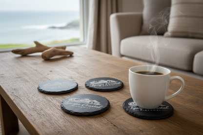 4 Round Slate Coasters, personalised with logo & name on a wooden coffee table in a Holiday Home by the sea