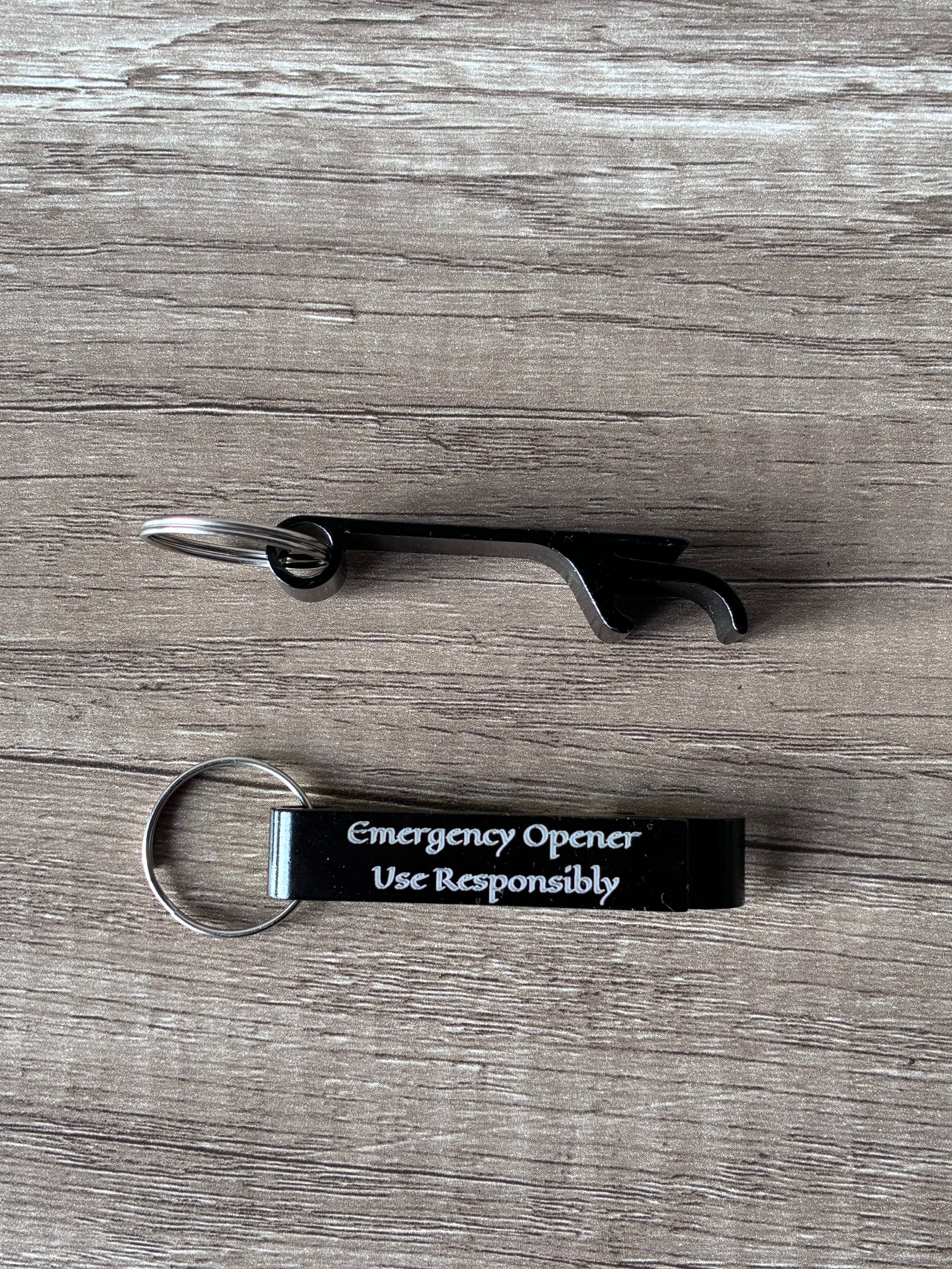 Bottle opener with keychain and 'Emergency Opener Use Responsibly' tag on a wooden surface