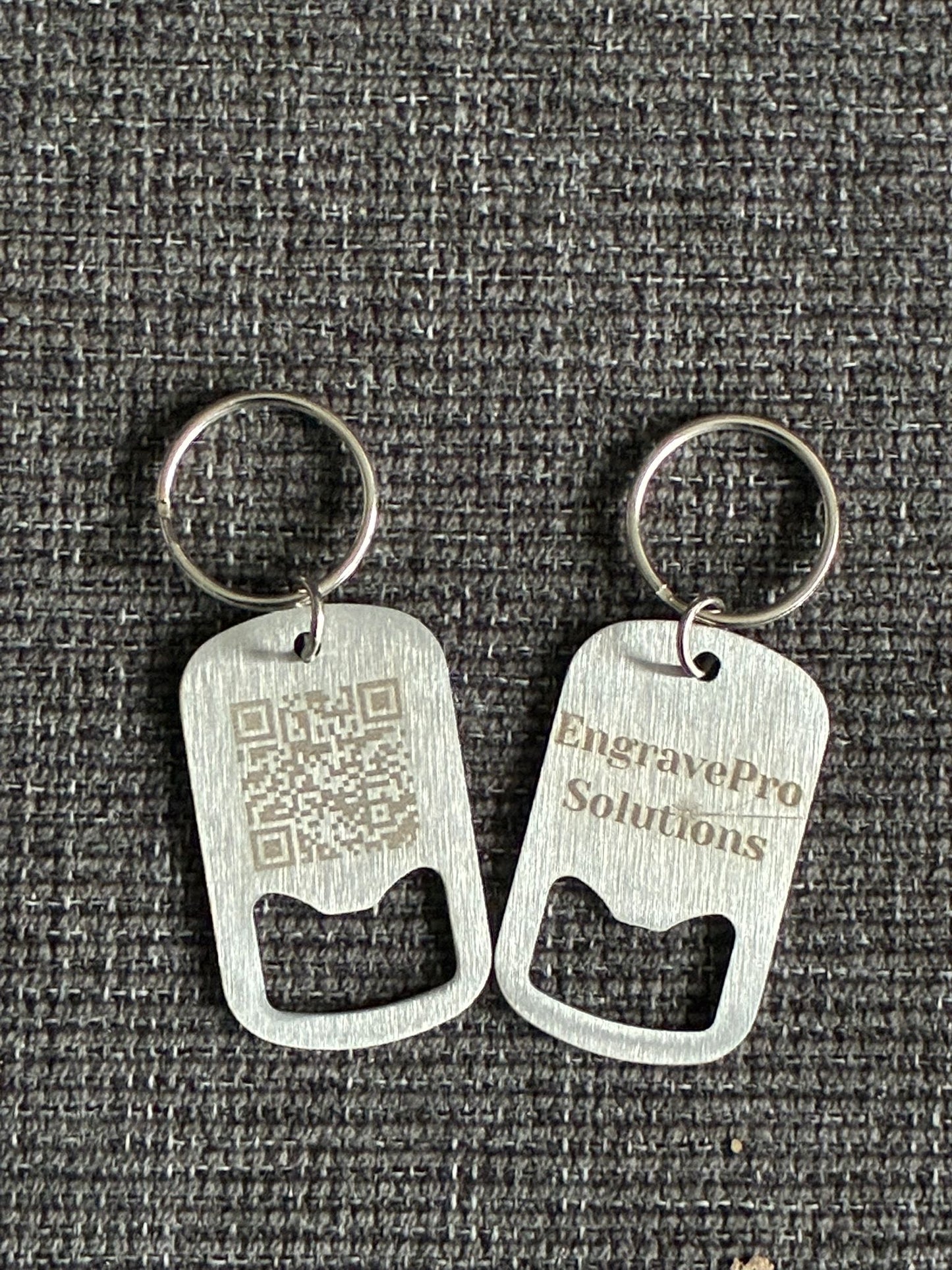 Two metal bottle opener keychains on a textured gray background