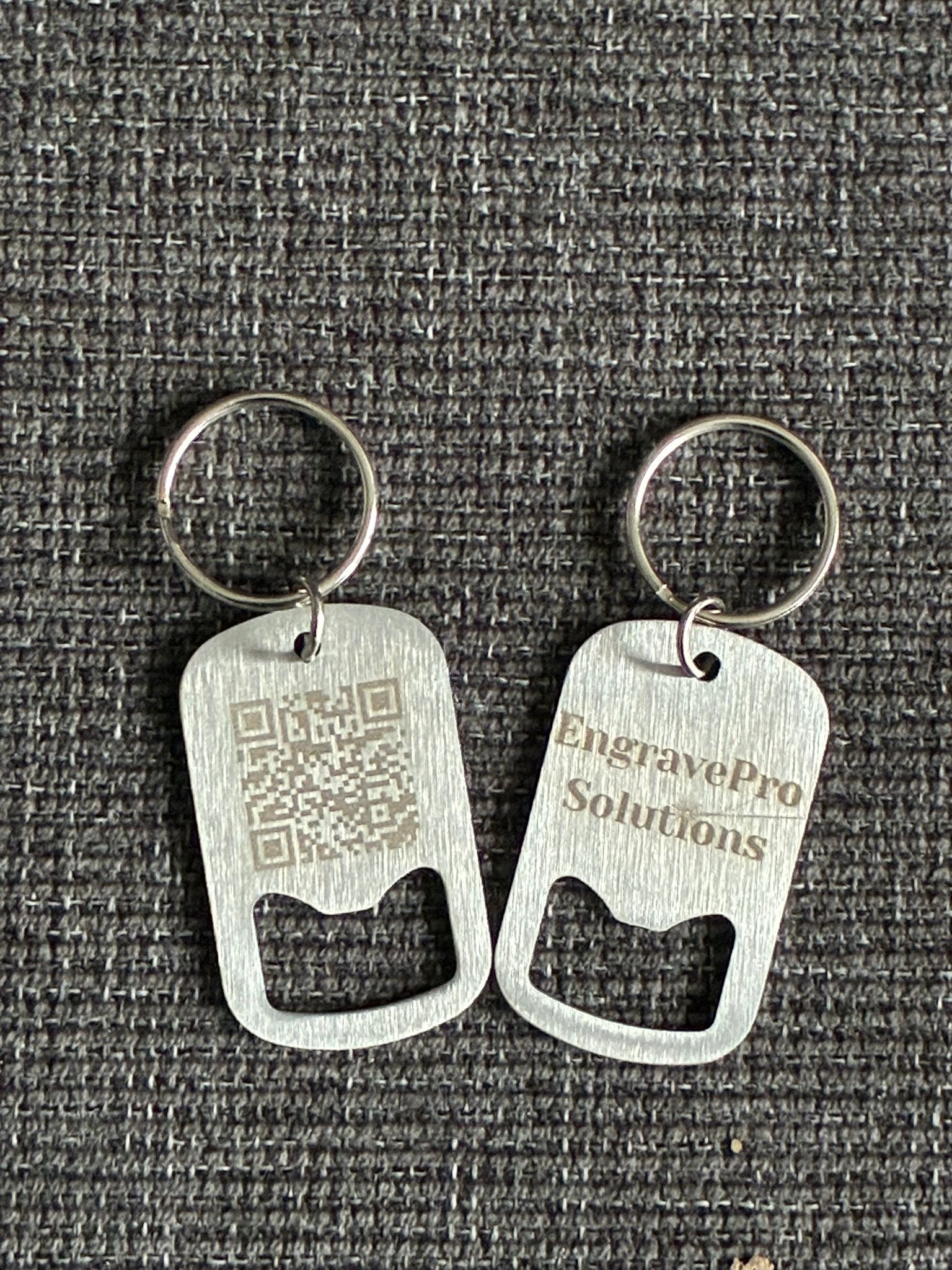 Two metal bottle opener keychains on a textured gray background