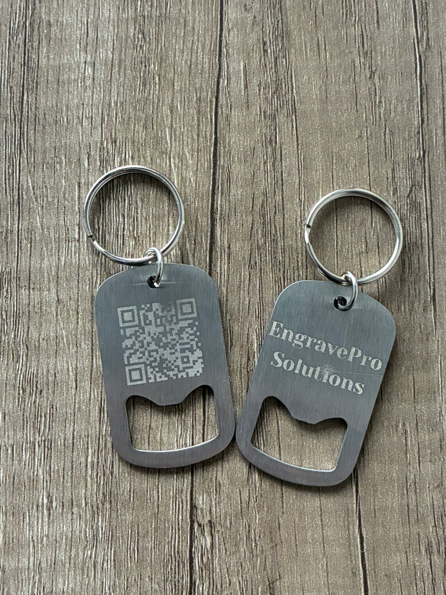 Two metal bottle opener keychains on a wooden surface with 'EngravePro Solutions' branding.