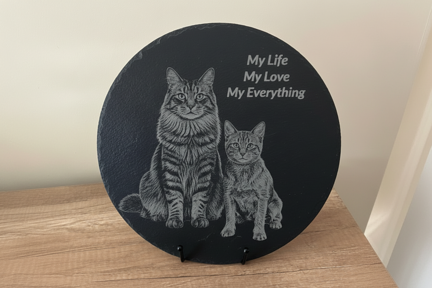 Round black slate with engraved image of two cats and text 'My Life, My Love, My Everything' on a wooden surface.
