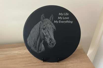 Round black slate with horse illustration and text on a wooden surface