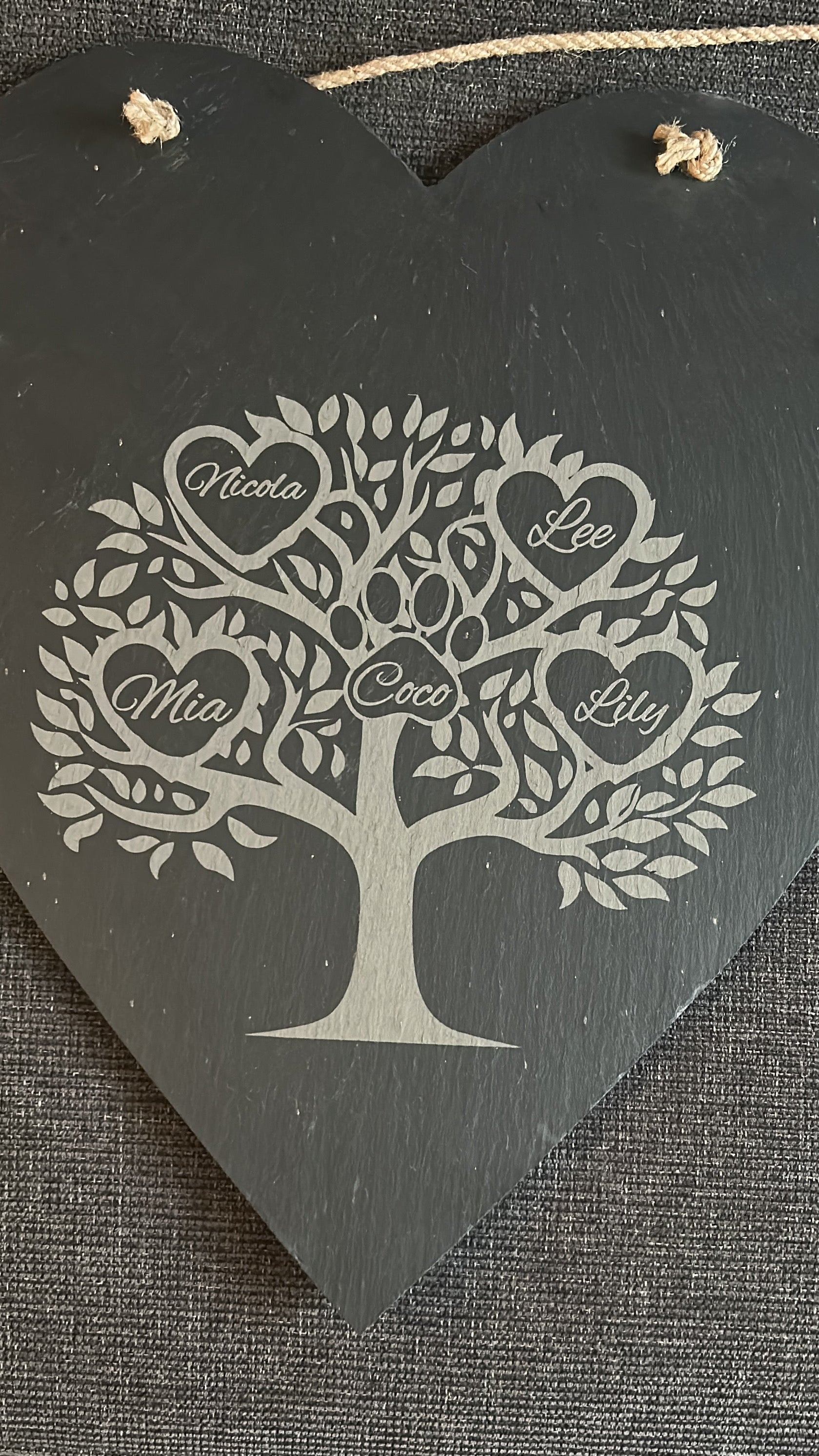 Decorative heart-shaped slate hanging board with tree design and engraved names ina heart on a textured surface.