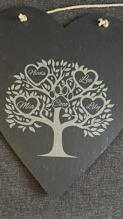 Decorative heart-shaped slate hanging board with tree design and engraved names ina heart on a textured surface.