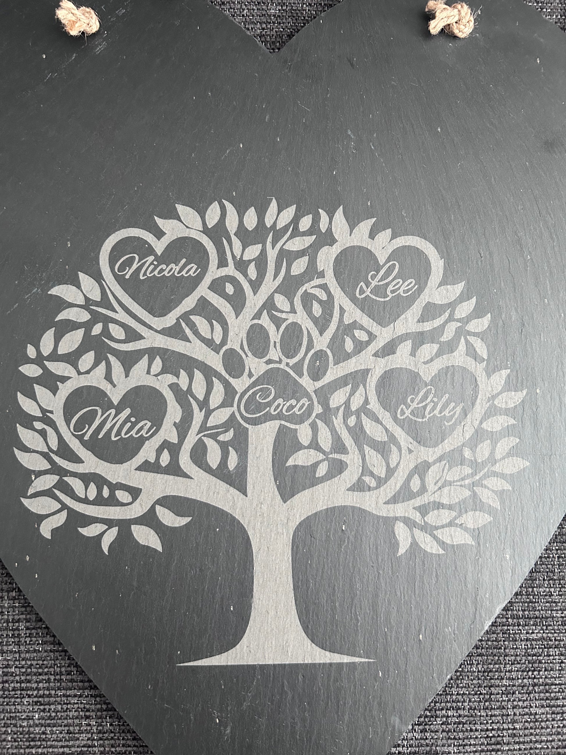 Decorative heart slate hanging board with family tree design and engraved names on a dark surface.