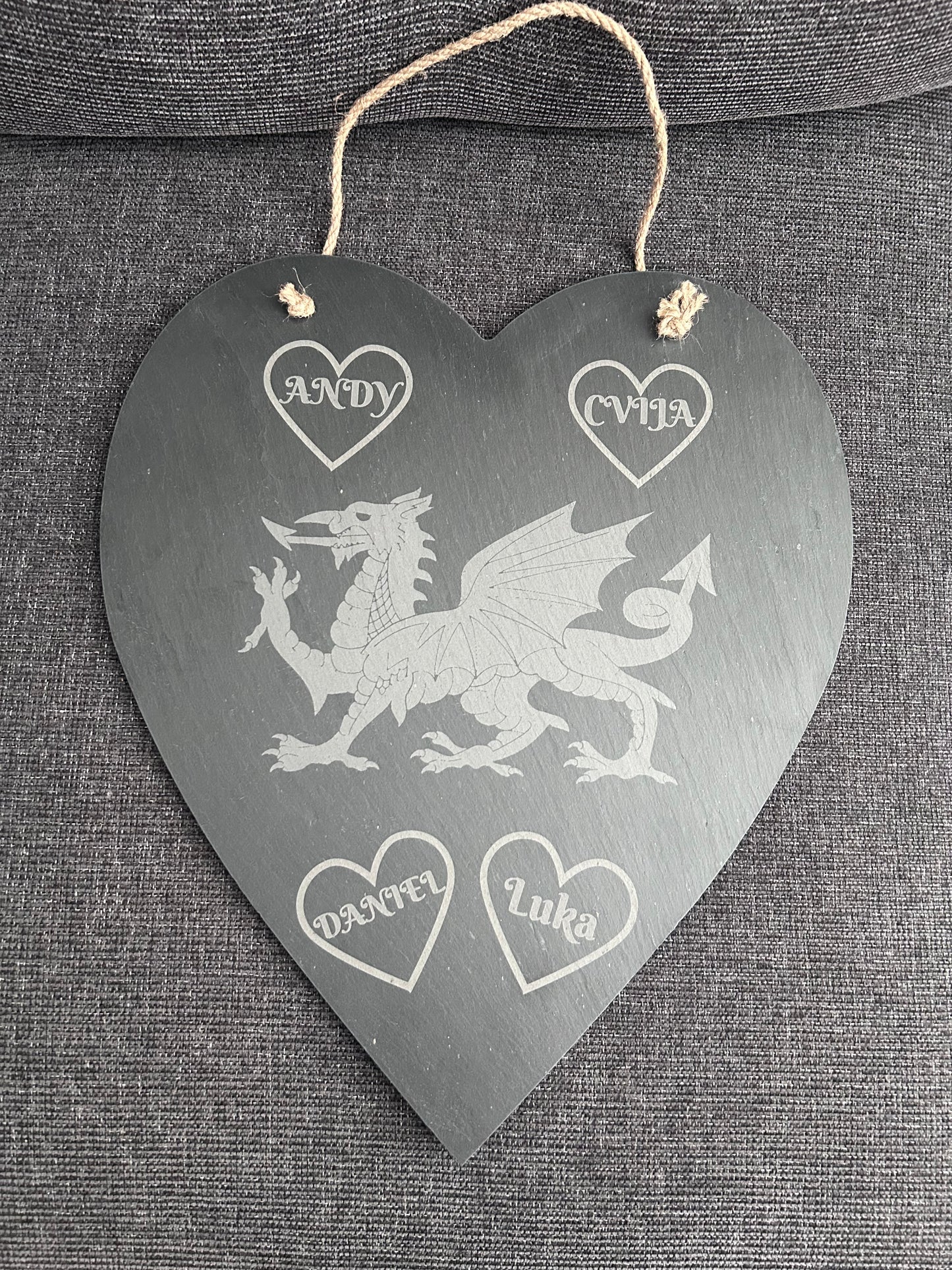 Heart-shaped slate plaque with engraved Welsh dragon design and names engraved in hearts on a grey fabric background