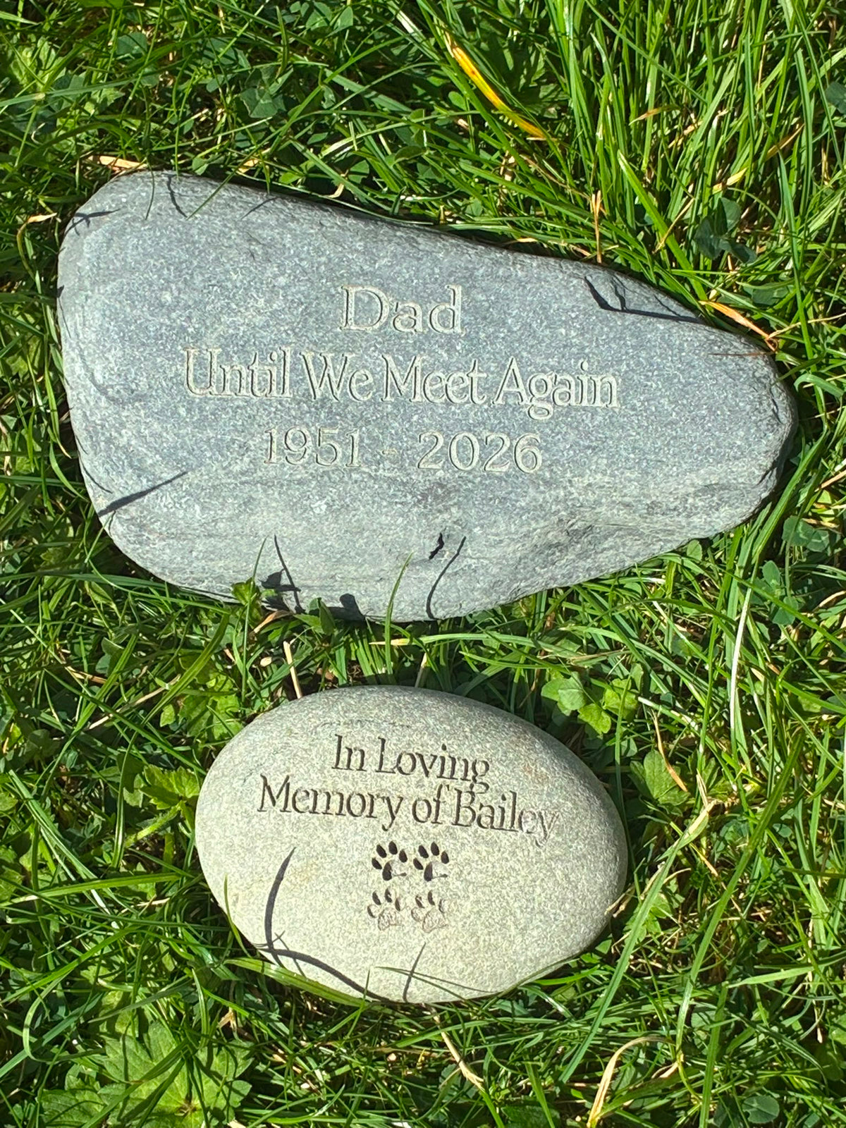 Two personalised natural memorial stones for a loved one and a pet, engraved and displayed together on grass