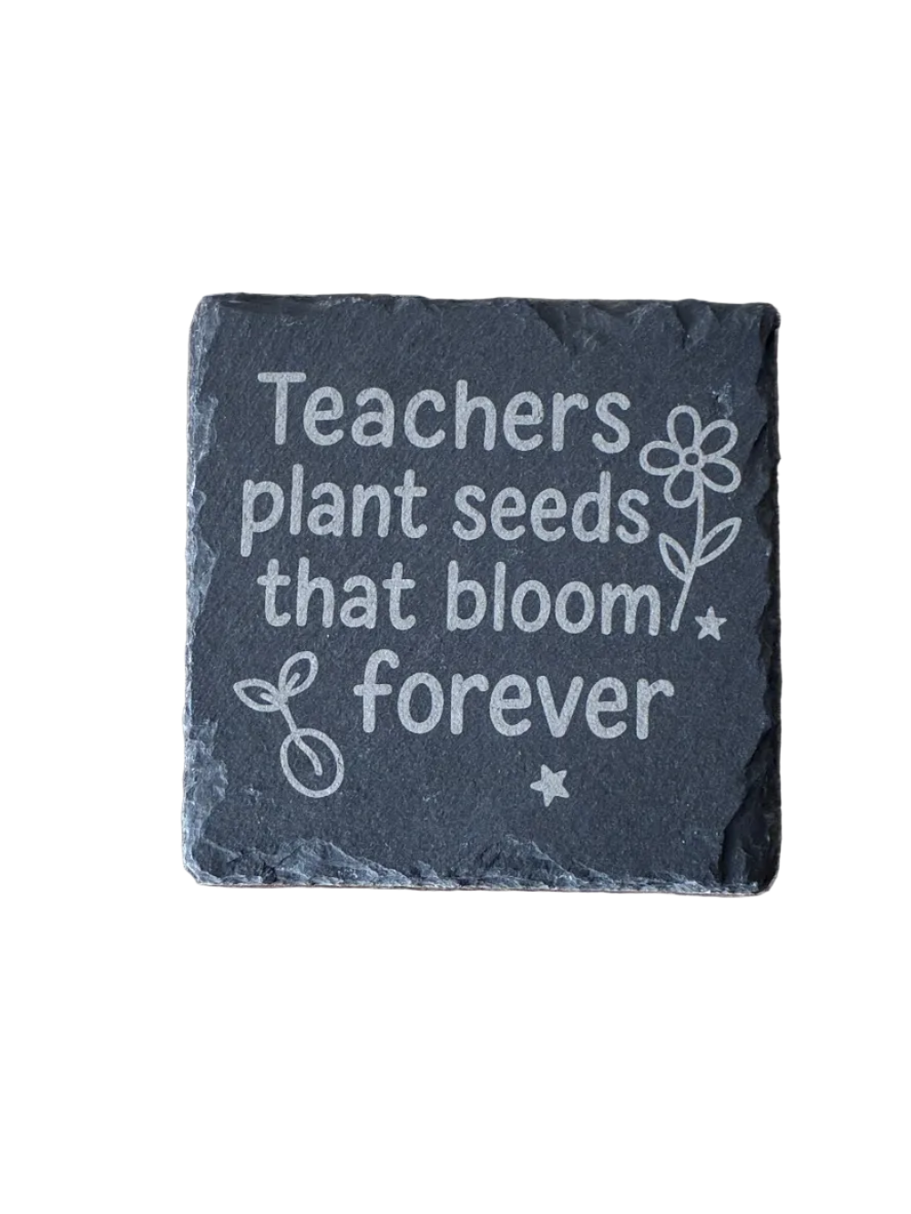Slate coaster with engraved text 'Teachers plant seeds that bloom forever' on a wooden surface