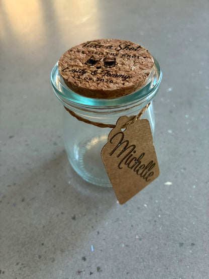 Clear glass wedding shot jar with an engraved cork lid and personalised kraft guest name tag.