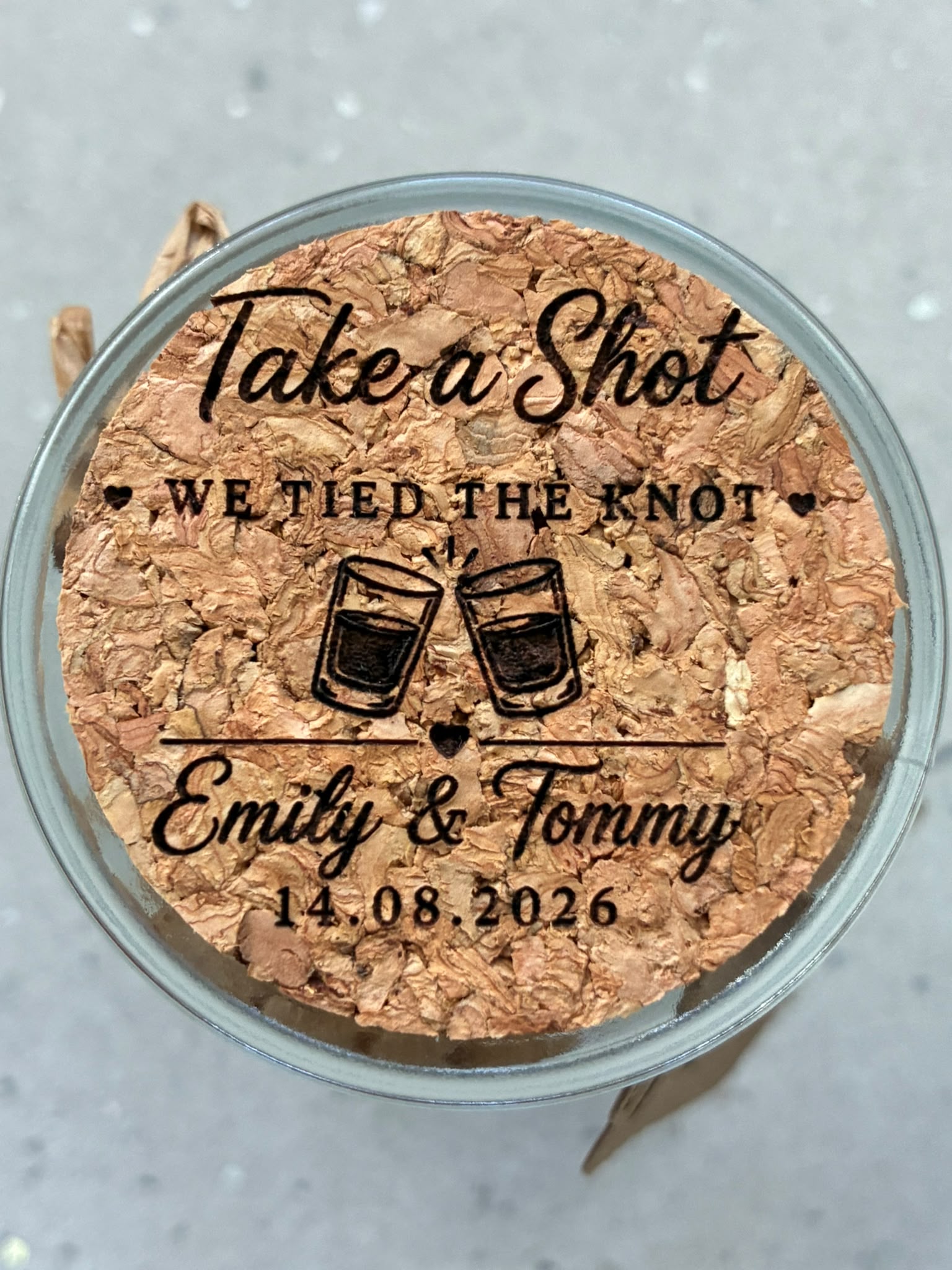 Close-up of a cork jar lid engraved with “Take a Shot, We Tied the Knot”, the couple’s names and wedding date.