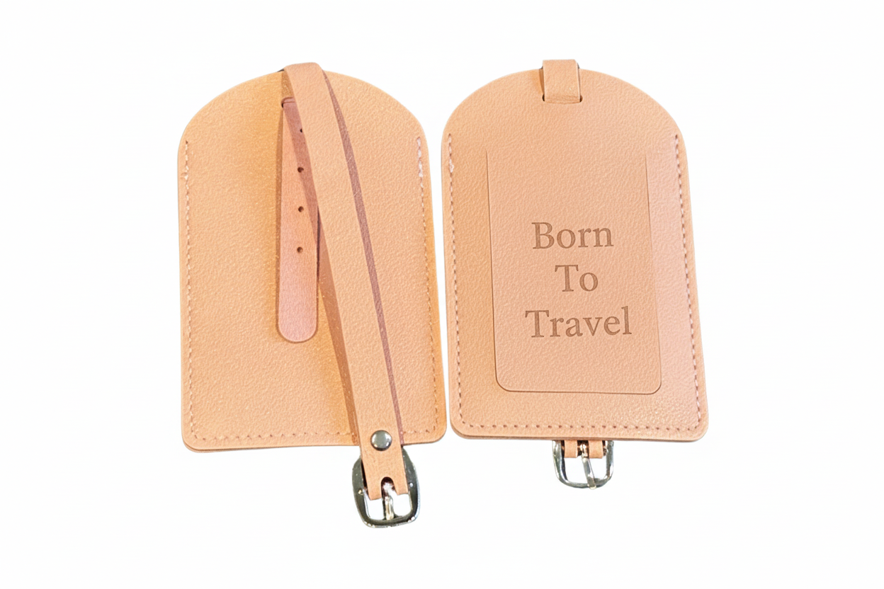 Two pink-colored luggage tags engraved with Born to Travel with straps on a white background