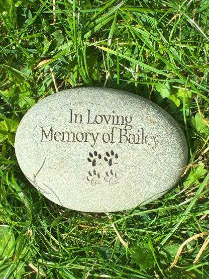 Natural stone engraved with In Loving Memory of Bailey and paw print design, displayed outdoors on grass