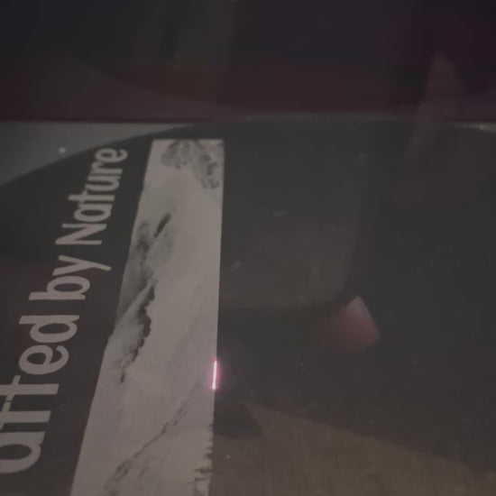 Laser engraving process on slate serving plate showing partial text 'Crafted by Nature' being etched onto the surface. Nuneaton UK