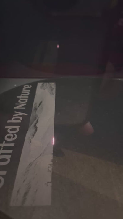Laser engraving process on slate serving plate showing partial text 'Crafted by Nature' being etched onto the surface. Nuneaton UK