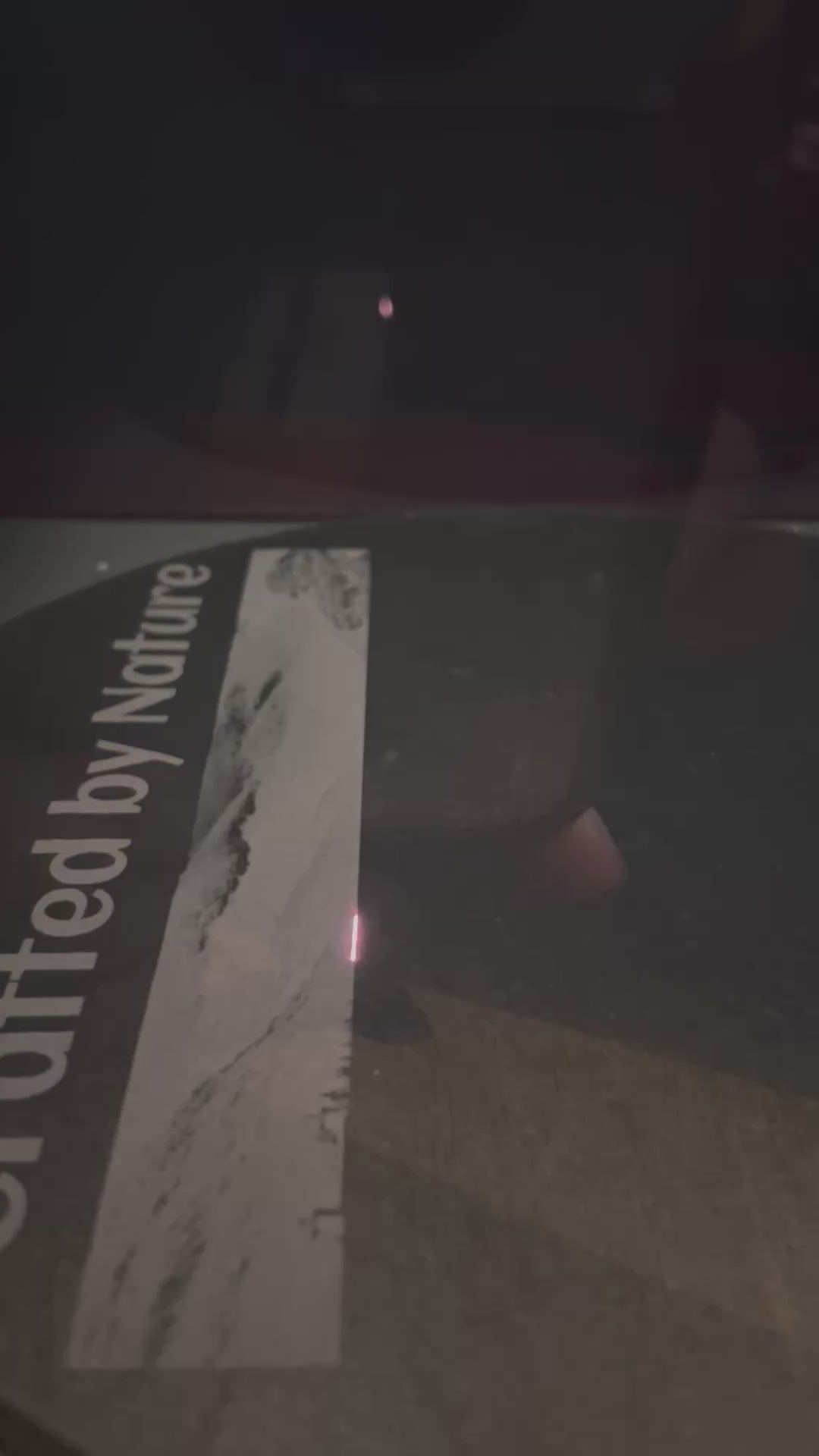 Laser engraving process on slate serving plate showing partial text 'Crafted by Nature' being etched onto the surface. Nuneaton UK