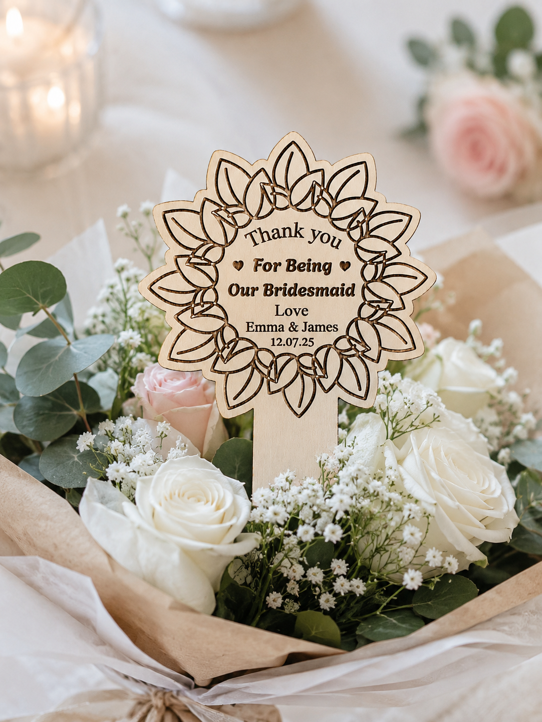 A personalised wooden wedding bouquet topper with an engraved floral wreath design and the text 'Thank you For Being Our Bridesmaid Love Emma & James 12.07.